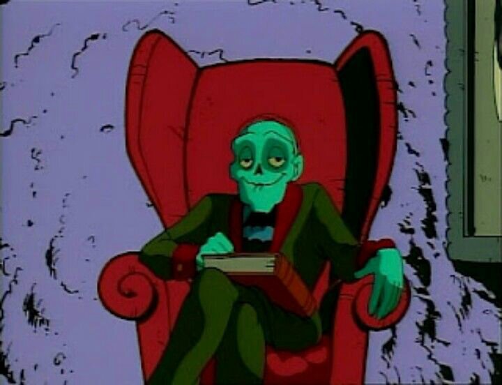 El guardián de la cripta en su versión dibujo animado de principios de los noventa sentando en un sillón, con un gran libro en su regazo y sonriendo.