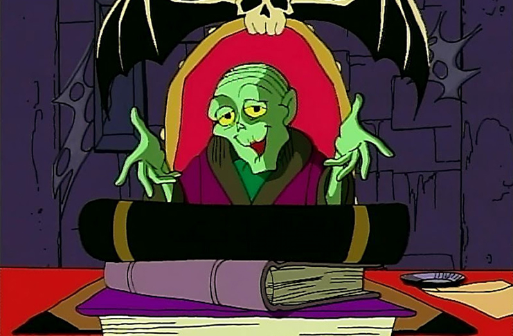 El guardián de la cripta en su versión dibujo animado de principios de los noventa sentado en una silla, en su escritorio, frente a una pila de libros, sonriendo y abriendo los brazos hacia el público lector.