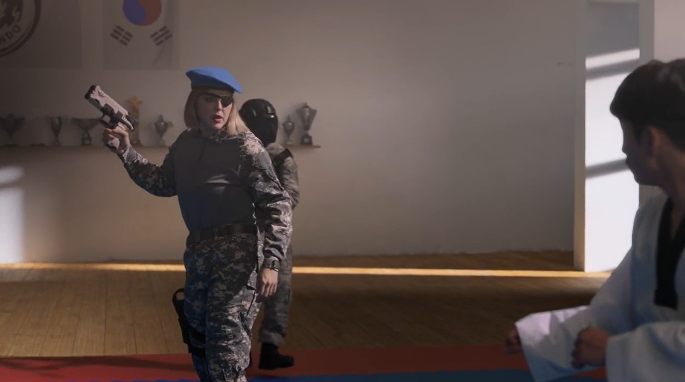 El gimnasio, con el chaval ahí, en el que entra una mujer de mediana edad, con un corte de pelo en bob, rubio, gorra azul y un parche en el ojo derecho.