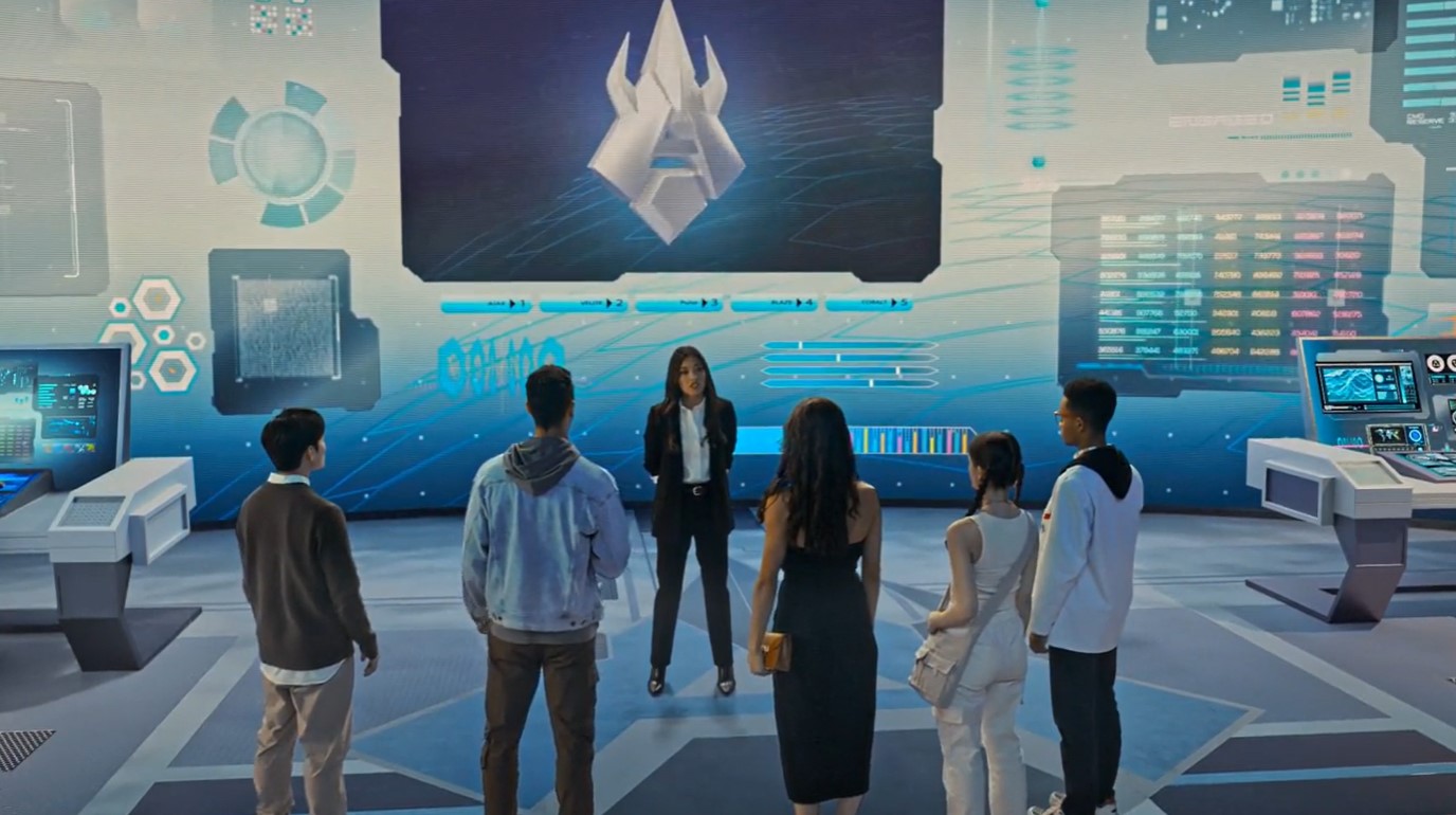 Los cuatro chavales de antes y el joven del gimnasio están de espaldas mientras la señora del traje está en el centro hablando, el 3D alrededor es de un laboratorio.