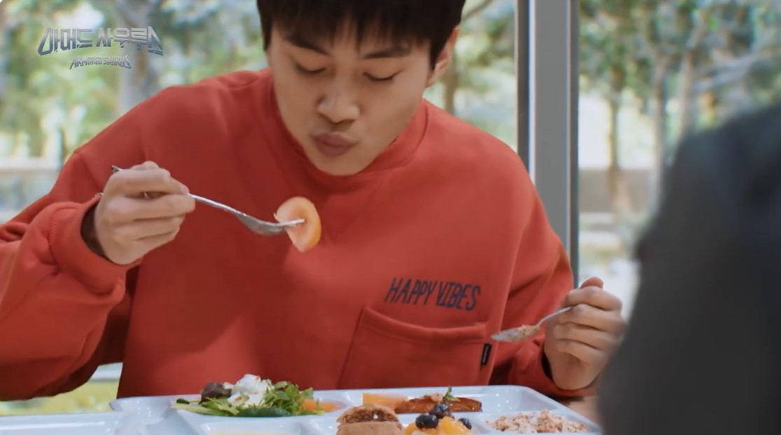 El chaval comiendo de una bandeja con distintas cosas de comida, a dos carrillos, con un tenedor a la derecha y un tomate, y a la derecha una cuchara con lo que parece una ensaladilla.