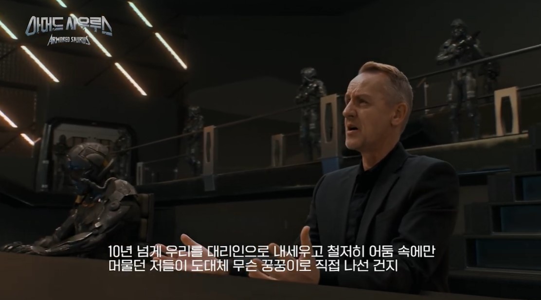 Imagen en la que vemos a un tipo en mitad de una habitación oscura, con un tipo en el centro. Le han puesto subtítulos en surcoreano.