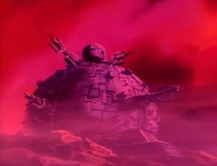 Imagen en la que vemos una cúpula, con forma de casco y mucha rayita, detrás de él hay una luminiscencia rojiza ominosa. Pero menos ominosa porque en lugar de Madrid lo que tiene son pinchos y un gran ojo encima, como corresponde a la Dimensión X.